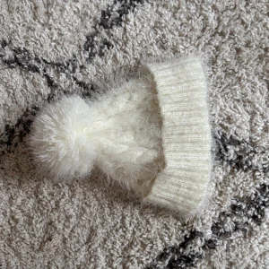 fluffig mössa - Mysig vit stickad mössa med fluffig tofs på toppen. Perfekt för kalla vinterdagar och ger en stilren look. Ribbad kant för extra komfort.