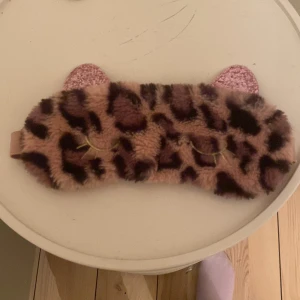 Leopardmönstrad sovmask från TOPModel - Mysig sovmask i leopardmönster med glittriga öron från TOPModel. Tillverkad i 100% polyester med ett elastiskt band för bekväm passform. Perfekt för en god natts sömn eller en avkopplande stund.