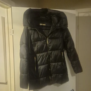 Svart pufferjacka från Mango - Snygg svart pufferjacka från MNG med dragkedja och praktiska fickor. Jackan har en stor huva och är perfekt för kyliga dagar. Den är långärmad och har en stilren design som passar till det mesta.