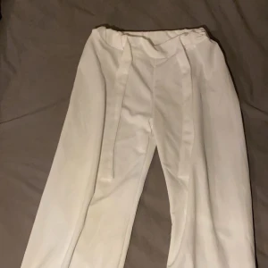 Vita kostymbyxor - Snygga vita kostymbyxor med hög midja och vida ben. Perfekta för en stilren look. Byxorna har en klassisk design med pressveck framtill.