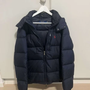 Mörkblå dunjacka från Polo Ralph Lauren - Snygg mörkblå dunjacka från Polo Ralph Lauren. Säljer då den inte passar mig längre. Pris kan diskuteras vid snabb affär.