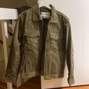 Olivgrön manchesterjacka från These Glory Days - Säljer en snygg olivgrön manchesterjacka från These Glory Days. Jackan har en klassisk krage, dragkedja framtill och praktiska fickor med lock. Perfekt för höst och vår!