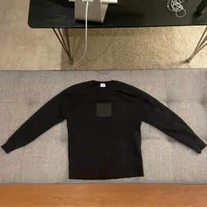 Svart tröja från C.P. Company - Snygg svart tröja från C.P. Company med en fyrkantig patch på bröstet. Perfekt för en stilren look.