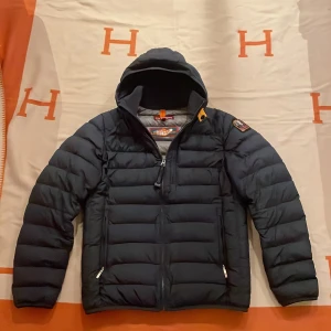 Svart pufferjacka från Parajumpers - Säljer en svart pufferjacka från Parajumpers. Jackan har en huva och dragkedja framtill. Den är superlätt och perfekt för kyliga dagar. Jackan är väldigt sparsamt använd. Storleken är Y-Mvilket är som en xs.