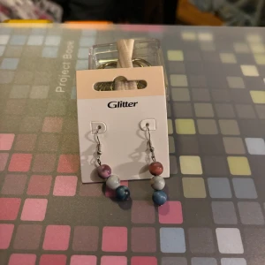 Flerfärgade örhängen - Snygga örhängen med flerfärgade pärlor i rosa, blått och grått. Perfekta för att ge en färgglad touch till din outfit. Hängande design med silverfärgad krok.