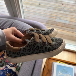 Leopardmönstrade sneakers med kardborreband - Snygga sneakers med leopardmönster, skorna har en vit sula samt namnet där bak. Har använt de en del men de är fortfarande i ett mycket bra skick!! Köpta för ett tag sedan för 1200kr, men pris kan disskuteras🙌
