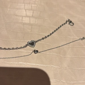 Silverfärgade armband  - Elegant silverfärgat armband med flera små hjärtan. Perfekt för att lägga till en romantisk touch till din outfit. Hjärtan är dekorerade med små stenar för extra glans.