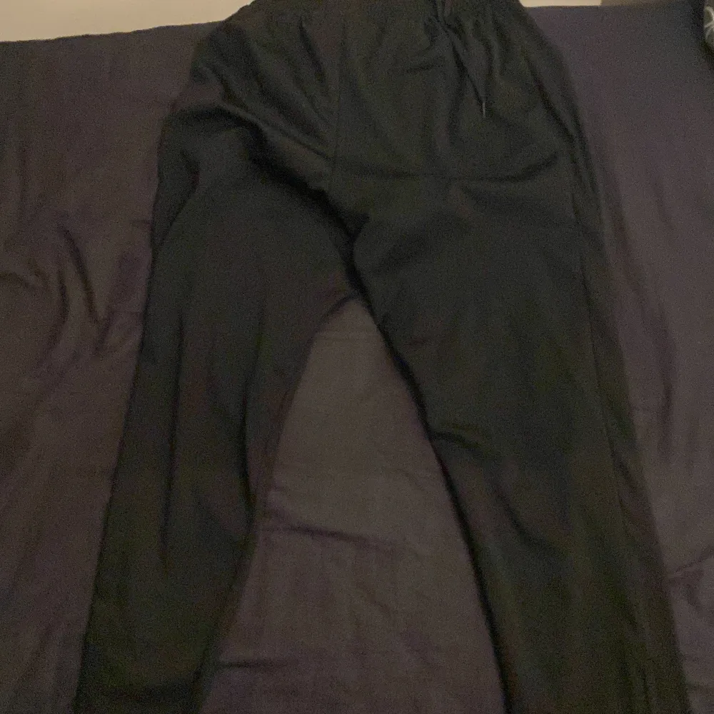 Säljer ett par svarta träningsbyxor från Nike med Dri-FIT-teknologi. Byxorna har en elastisk midja och en dragkedja vid bensluten för extra komfort. Perfekta för träning och sportaktiviteter. Väldigt bra skick, vid fler frågor kom dm!. Farkut & Housut.