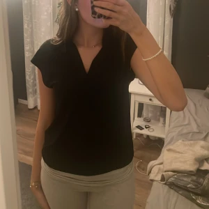 Svart blus från H&M - Snygg svart blus från H&M i en elegant design. Blusen har en v-ringad hals och korta ärmar, perfekt för både vardag och fest. Tillverkad i ett mjukt och bekvämt material.😍😍