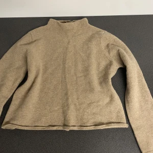 Beige tröja från Arnie Says - Säljer en stilren beige tröja från Arnie Says i en mjuk blandning av lammull och kashmir. Tröjan har en hög krage och långa ärmar, perfekt för kyligare dagar. Enkel och elegant design som passar till det mesta.