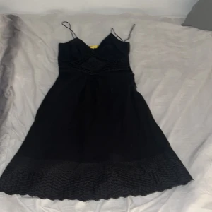 Svart klänning med spetsdetaljer - Elegant svart klänning med smala axelband och vacker spetsdetalj vid midjan. Perfekt för en stilren look.