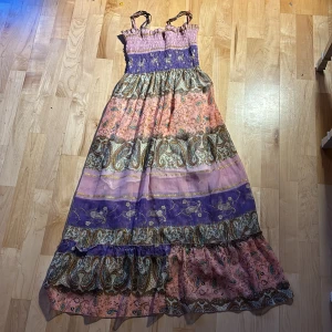 Färgglad långklänning med mönster.  - Charmig långklänning med ett färgglatt och bohemiskt mönster i rosa, lila och grönt. Klänningen har smala axelband och volangdetaljer upptill. Perfekt för en somrig dag med sin luftiga design. Pris kan diskuteras!