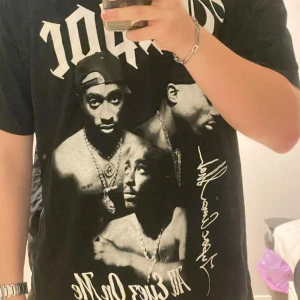 Svart T-shirt med 2Pac-tryck från Pull&Bear - Cool svart T-shirt från Pull&Bear med stort tryck av 2Pac på framsidan. Perfekt för dig som gillar hiphop och streetwear. T-shirten har en normal passform och är kortärmad.