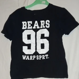 Svart t-shirt med tryck från WA. Barn storlek 122-128  - Cool svart t-shirt från WA med stort vitt tryck 'BEARS 96 WARP SPRT.' på framsidan. Tillverkad i ekologisk bomull, perfekt för en avslappnad stil..  Barn storlek 122-128 