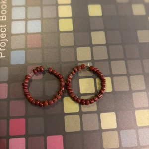 Vinröda pärlörhängen - Snygga vinröda örhängen med pärlor i en cirkulär design. Perfekta för att ge en färgklick till din outfit. Passar både till vardag och festliga tillfällen.