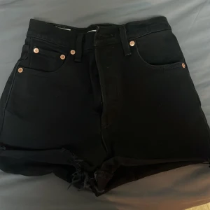 Svarta jeansshorts från Levi's - Snygga svarta Ribcage shorts från Levi's Premium. De är högmidjade med klassisk femficksdesign och knappgylf. Perfekta för en cool och avslappnad stil.