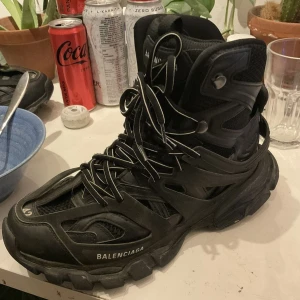 Balenciaga track hike - Säljer ett par svarta Balenciaga sneakers med robust design och snörning. Skorna har en modern och chunky stil med Balenciaga-logga på sidan. Perfekta för dig som gillar en statement-look.