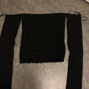 Svart tubtopp från Gina Tricot - Snygg svart tubtopp från Gina Tricot i storlek XS. Toppen har långa ärmar och en fin volangdetalj vid nederkanten. Perfekt för en stilren look. aldrig väntar utan prislapp