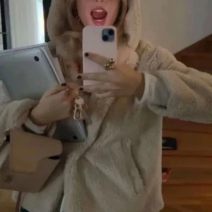 Beige teddyjacka med huva - Mysig beige teddyjacka med huva, perfekt för kyliga dagar. Jackan har en avslappnad passform och stängs med knappar framtill. Den är både stilren och bekväm, vilket gör den till ett mångsidigt plagg i garderoben.