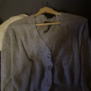 Grå ribbad kofta från BIKBOK - Säljer en stilren grå ribbad kofta från BIKBOK i storlek XS. Koftan har en v-ringad design med knappar framtill och långa ärmar. Perfekt för lager-på-lager under kyligare dagar. Finns en liten dekfekt som knappast syns en liten rosa fläck annars jätte fin.