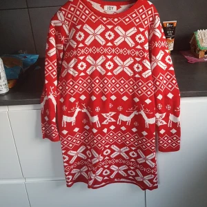 Röd jultröja från JDY - Säljer en mysig röd jultröja från JDY med ett festligt mönster av vita renar och snöflingor. Tröjan har långa ärmar och är perfekt för julfirandet. Den är både varm och stilren, idealisk för kalla vinterdagar.