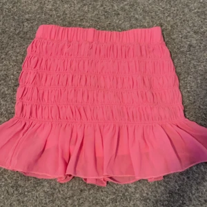 Rosa kjol från Shein - Säljer en söt rosa kjol från Shein med volangdetaljer. Kjolen har en elastisk midja och är perfekt för en färgglad look. Den är kort och har en lekfull design som passar bra till sommaren.