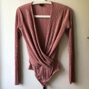 Rosa omlott bodysuit - Snygg rosa omlott bodysuit med ribbad textur och långa ärmar. Perfekt för en stilren look.