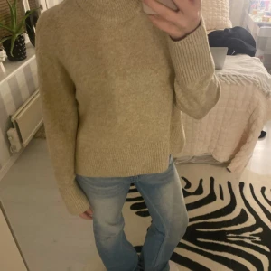 Beige stickad polotröja - Säljer en mysig beige stickad polotröja med ribbade detaljer. Tröjan har långa ärmar och en bekväm passform som passar perfekt för kyligare dagar. Perfekt för en stilren och avslappnad look.