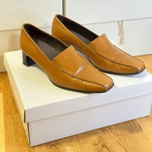 Bruna läder skor - Snygga bruna läder skor i skinn med en låg klack. Perfekta för en stilren look. De har en spetsig tå och en elegant design som passar till många tillfällen.