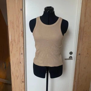 Beige ribbad linnetopp - Säljer en stilren beige ribbad linnetopp. Den är ärmlös med en rund halsringning och har en tight passform. Perfekt för varma dagar eller som lager under en tröja.