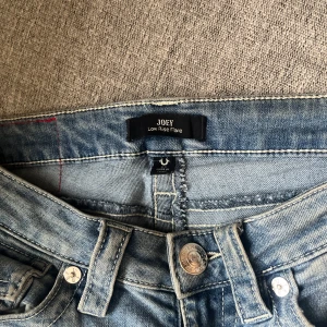 Blå jeans från True Religion - Snygga blå jeans från True Religion med låg midja och flare-stil. De har klassiska femfickor och en knappgylf. Perfekta för en avslappnad look. Vill tillläga ut på bilderna är dem inte tvättade men på sita bilden ser man hur den ser ut nytvättade, sedan är dem lite slitna i slutet av byxan (längst ner) ocksp ett litet hål på knät💓säljer för 500kr me tanke på hålet orginal pris 1 299kr
