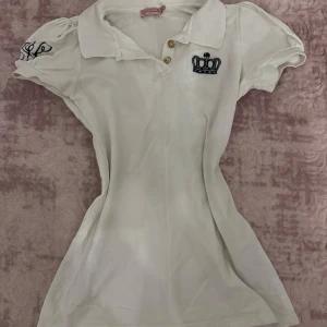 Vit polotopp från Juicy Couture - Säljer en stilren vit polotopp från Juicy Couture med korta puffärmar och en broderad krona på bröstet.        Skriv för fler frågor 💗.  