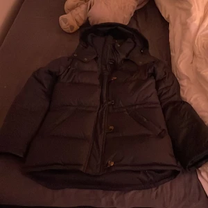 Marinblå dunjacka från Boomrang - Säljer en svart dunjacka från Boomrang, modell 'The Authentic 7036 Classic Down Jacket'. Jackan har långa ärmar och knappar framtill. Perfekt för kalla dagar med sin varma och vadderade design. Är super skön, har använt ett fåtal gånger och har nästintill inga tecken på användning. Pris kan diskuteras vid snabb affär! 💕