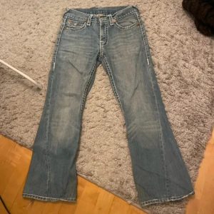 True religion jeans white stitch - Blå Trueys med vit söm, asfeta! Dom är bootcut, inte så jätte lågmidjade men ändå coola. De är i storlek 30 men är är mått som beskriver bättre: Midja (rakt över)- 40cm Innerben längd- 72cm Ytterben längd- 98cm Har defekt vid hälarna från heeldrag, men det går att se över Skriv för fler bilder eller om ni har frågor!