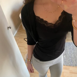 Svart bolerotopp med knapp - Säljer en stilren svart bolerotopp med en stor knapp framtill. Perfekt för att lägga till en extra touch till din outfit. Den har trekvartsärmar och en enkel design som gör den lätt att matcha med andra plagg.