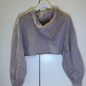 Ljuslila croppad hoodie - Säljer en snygg ljuslila croppad hoodie med huva och dragsnören. Perfekt för en avslappnad stil. Den har långa ärmar och en lös passform som ger en bekväm känsla.