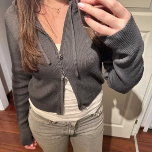 Grå ribbad ziphoodie - Säljer en snygg grå ribbad hoodie från Monki i storlek S. Den har en justerbar dragkedja framtill och långa ärmar. Perfekt för en avslappnad stil. Aldrig använd, prislapp kvar🪩