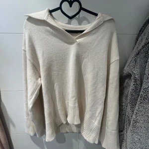 Vit stickad tröja från Gina Tricot - Säljer en stilren vit stickad tröja från Gina Tricot. Tröjan har en unik krage och långa ärmar med ribbade muddar. Perfekt för kyligare dagar och ger en avslappnad look.