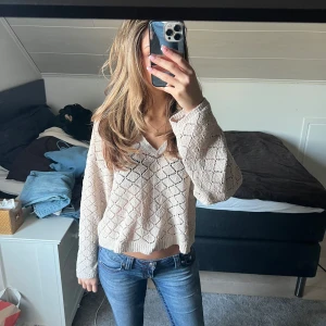 Beige stickad tröja från Pull&Bear - Säljer en snygg beige stickad tröja från Pull&Bear. Tröjan har ett fint hålmönster och en v-ringad design. Den är croppad och har långa ärmar, perfekt för en avslappnad stil. Passar bra till jeans eller kjol. 🌟