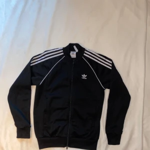 Adidas Superstar Track Top - Adidas Superstar Track Top – Black with White Stripes A stylish track top from the Adidas Superstar series in black with the classic white stripes. Perfect for a sporty look or everyday style! Size: S Color: Black with white stripes Condition: Good condition, lightly used Brand: Adidas Superstar – iconic design and high quality. Feel free to ask if you want more pictures or details!
