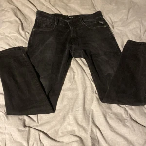 Svarta jeans från Replay - Snygga svarta jeans från Replay, modell Anbass. De har en klassisk femficksdesign med dragkedja och knapp framtill. Perfekta för en stilren look. De har blivit uppsydda så sitter mer som mellan 28 och 30 på längden. 