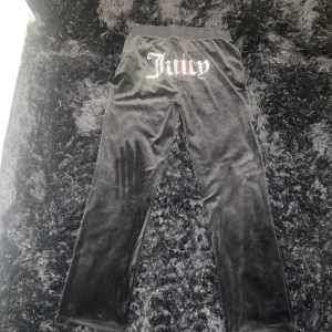 Svarta Juicy Couture byxor L - Snygga svarta byxor från Juicy Couture i mjukt sammetstyg. Byxorna har en glittrande strassdetalj med texten 'Juicy' på baksidan och en liten 'JC' på framsidan. Perfekta för en glamorös look. Byxornas storlek är L men passar även M och S. Använt 1-2 gånger. Nyskick nästan. Byxorna ska tvättas innan jag levererar dem. 