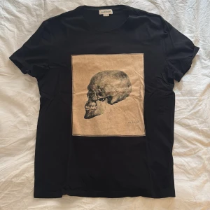  Alexander McQueen T-shirt - Snygg svart t-shirt från Alexander McQueen med ett stort dödskalletryck på framsidan. Tillverkad i Italien, köpt via Farfetch. Klassisk passform. Nypris 1700kr