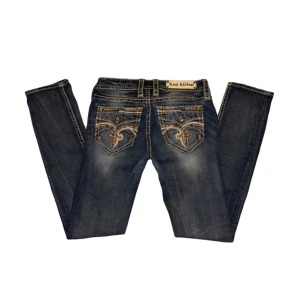 Blå jeans från Rock Revival - Snygga blå jeans från Rock Revival med unika broderade detaljer på bakfickorna. De har en straight passform och är tillverkade i slitstarkt denim. 