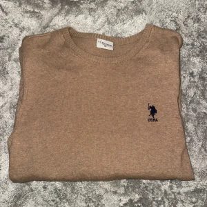 Beige tröja från U.S. Polo Assn. - Säljer en stilren beige tröja från U.S. Polo Assn. med rund halsringning och ett diskret broderat logotyp på bröstet. Perfekt för en avslappnad look. Tröjan har långa ärmar och är tillverkad i ett mjukt material.