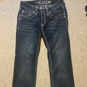 Mörkblå jeans från Camp David - Snygga mörkblå jeans från Camp David med kontrasterande vita sömmar. De har en klassisk femficksdesign och knappar på bakfickorna. Dem skulle passa M-L