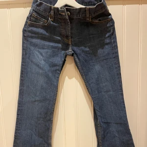 Blå jeans med broderade bakfickor - Snygga blå jeans med unika broderade detaljer på bakfickorna. De har en klassisk femficksdesign och en knapp- och dragkedjestängning framtill. Perfekta för en avslappnad stil.