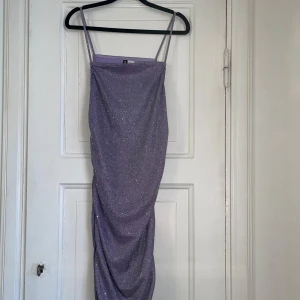  glittrig klänning - HELT NY prislapp kvar, snygg lila klänning med glittrigt material och smala axelband. Perfekt för en kväll ute eller en speciell tillställning. Klänningen har en figurnära passform och är tillverkad i ett glittrigt tyg som fångar ljuset fint 