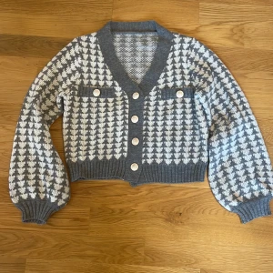 Grå&  vit kofta med knappar - Säljer en snygg grå och vit kofta med ett klassiskt rutigt mönster. Koftan har långa ärmar och knappar framtill samt dekorativa fickor med knappar. 