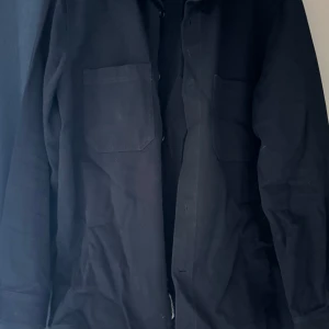 Svart overshirt med fickor från arket - Säljer en stilren svart overshirt med två bröstfickor. Perfekt för lager-på-lager och har en klassisk look. Passar bra till både casual och mer uppklädda tillfällen.